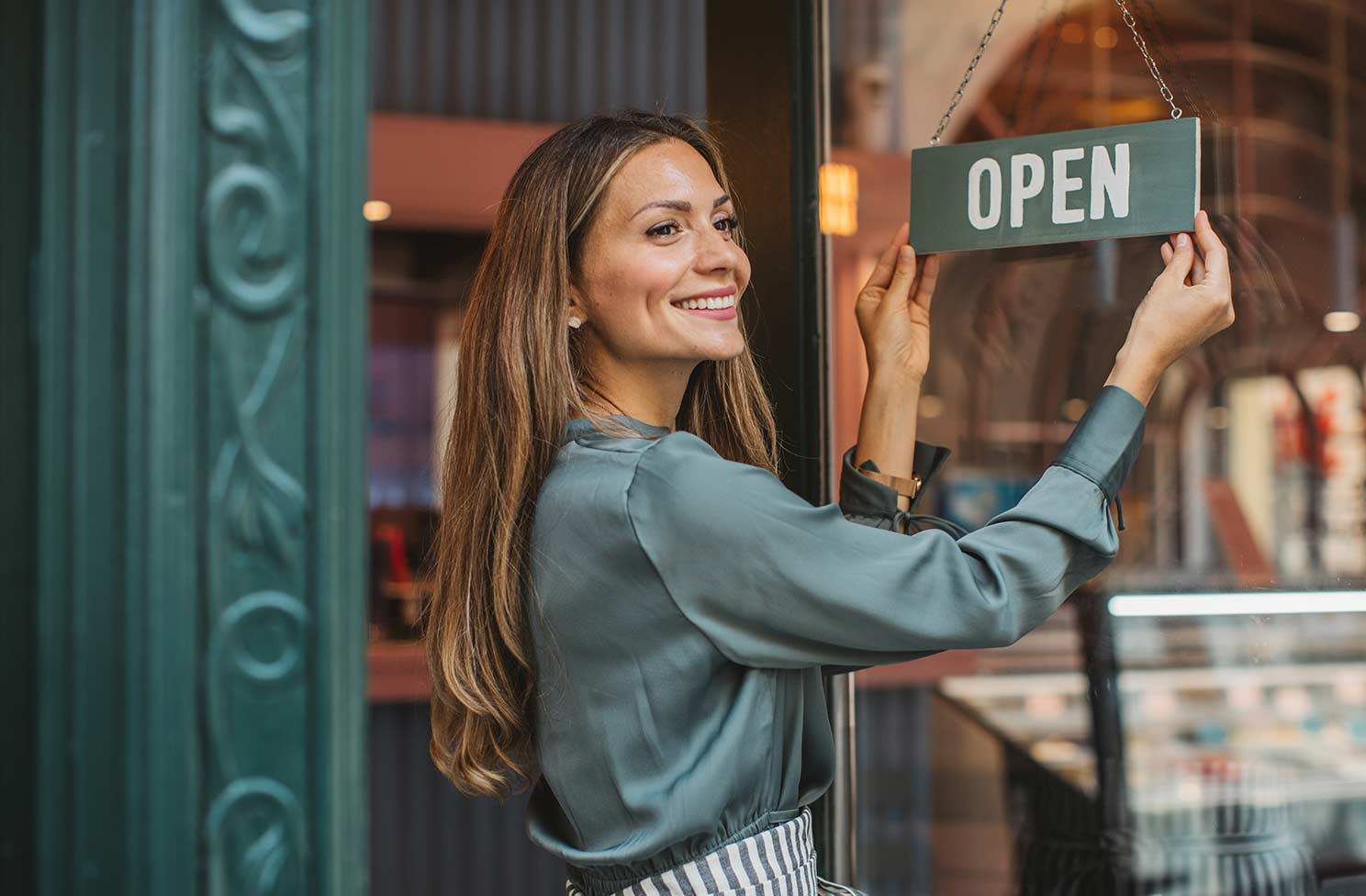 A woman smiling as she turns her shop sign to Open